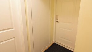 Un couloir étroit, avec une porte blanche fermée sur la droite et une porte blanche fermée sur la gauche.