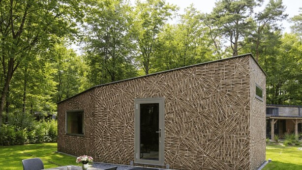 Un edificio moderno con diseño geométrico, fachada estampada, una puerta y un pequeño patio con mesa y sillas.