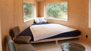 Un dormitorio con una cama, dos ventanas, una silla y una mesita.