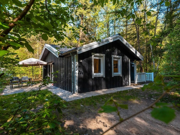 En stuga byggd av trä med en veranda, en täckt sittplats och en grusgång som leder fram till entrén.