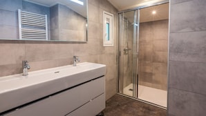Un baño moderno con un espejo grande, dos lavamanos y una ducha con cerramiento de vidrio.