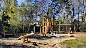 Un parque infantil con tobogán y columpios en un área boscosa.