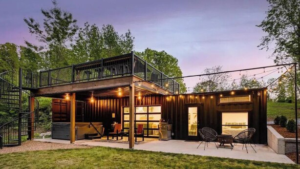 Une cabane en bois à deux étages, dotée d’un balcon, d’un espace salon extérieur et de guirlandes lumineuses.