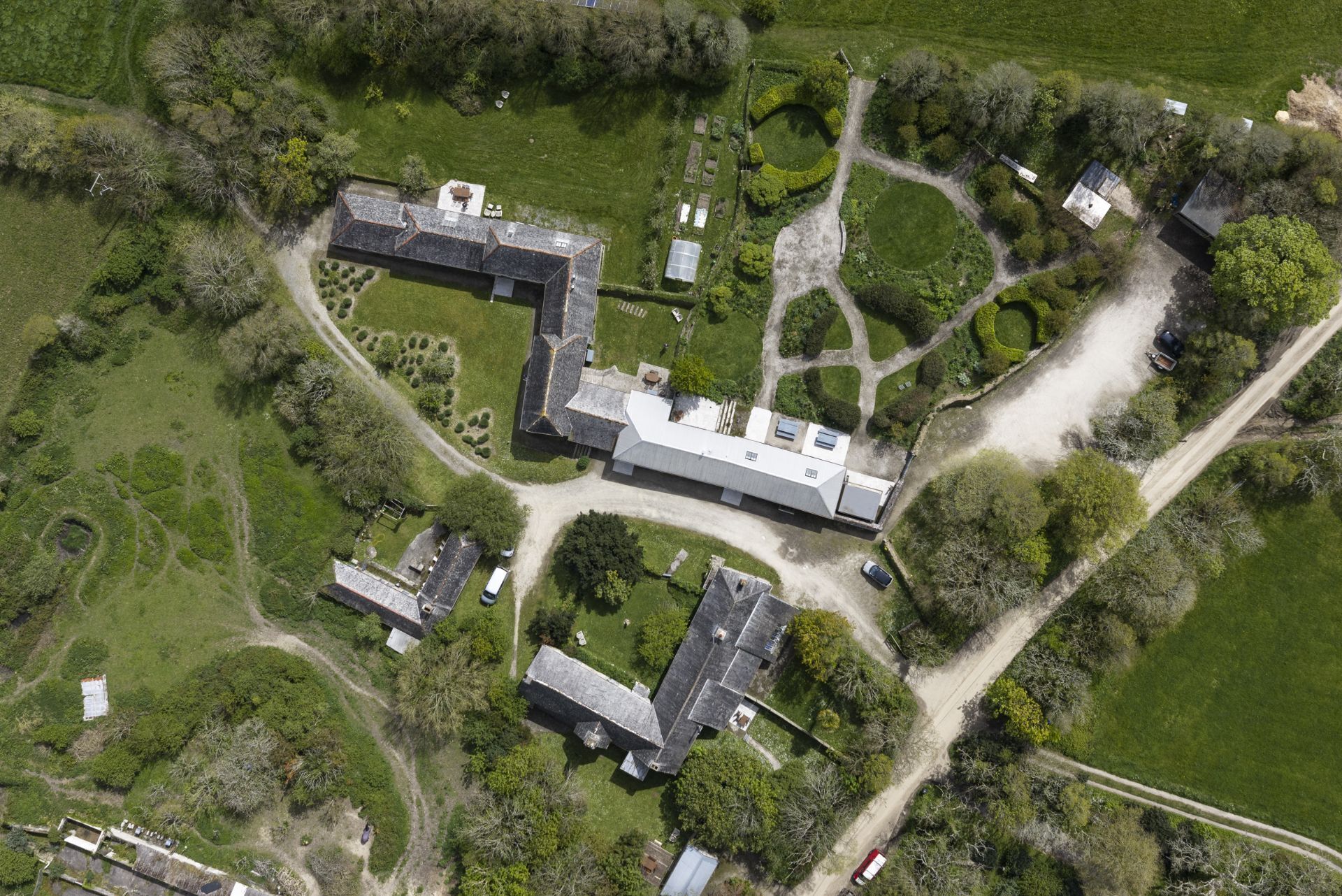 An aerial view of a property with multiple buildings, a large central structure, and surrounding greenery.