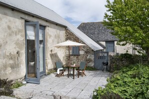 Une terrasse avec une table et des chaises, une porte et un petit espace jardin.