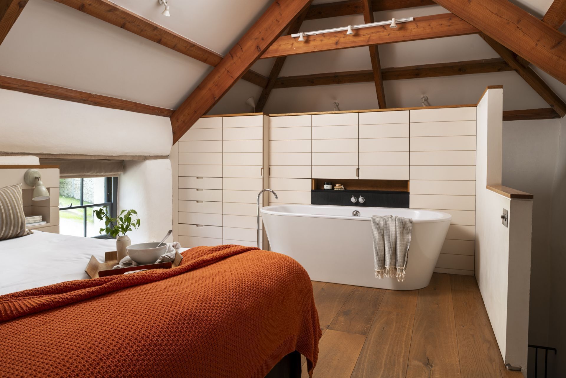 Een slaapkamer met een groot bed, een nachtkastje met een lamp en een raam met uitzicht.