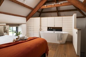 A bedroom with a large bed, a bedside table with a lamp, and a window with a view. - Howthere Barn - sleeps 2 guests  in 1 bedroom (Helford)