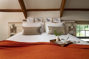 Une chambre à coucher avec un lit, des oreillers, un plateau avec un bol et une cuillère, une plante et des tableaux encadrés au mur.