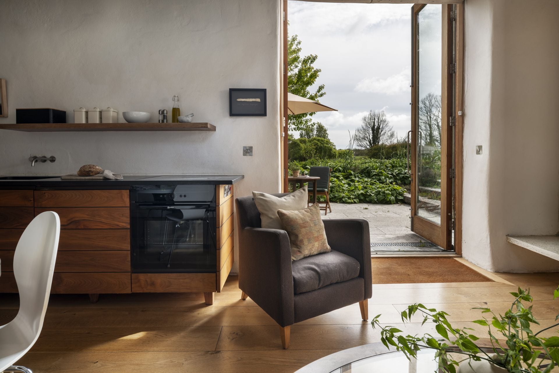 Eine moderne Küche mit Einbauofen, eine Essecke mit Stuhl und Tisch sowie ein Blick ins Freie durch eine Glastür.
