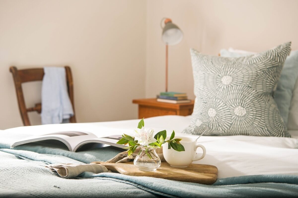 A neatly made bed with a book, a cup, and a small vase with flowers.