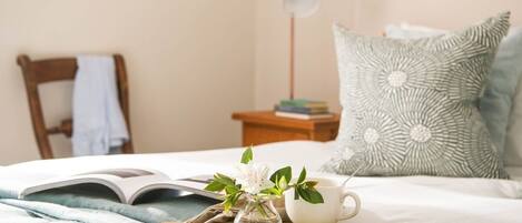 A neatly made bed with a book, a cup, and a small vase with flowers.