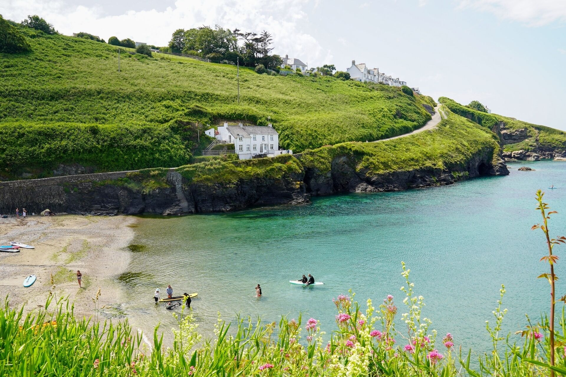 Un paysage côtier avec un bâtiment blanc sur une colline verdoyante, une mer bleue et limpide, et une côte rocheuse.