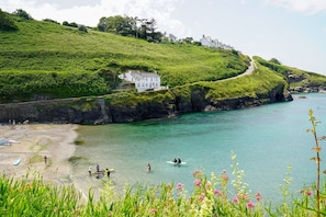 A coastal landscape with a white building on a grassy hill, a clear blue sea, and a rocky shoreline. - Jasmine Cottage - sleeps 3 guests  in 2 bedrooms (Port Gaverne)