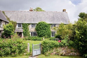 Ein Steinhaus mit geneigtem Dach, ein Garten mit blühenden Pflanzen und ein Holztor.