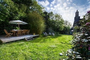 Ein üppiger Garten mit einer Holzterrasse, Gartenmöbeln und einem Gazebo.