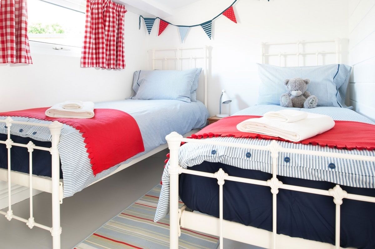 A bedroom with two beds, each with a red and blue striped bedspread, white headboards, and a teddy bear on the right bed.