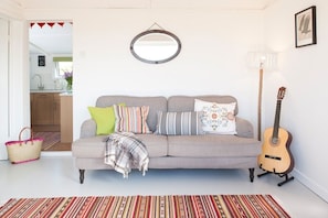 A living room with a grey sofa, colorful pillows, a guitar, and a striped rug. - Lighthouse View - sleeps 4 guests  in 2 bedrooms (Hayle)