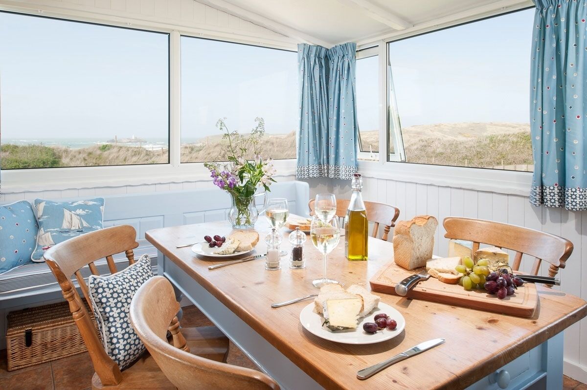 A dining area with a table set for two, featuring a bottle of olive oil, a bottle of white wine, a plate of cheese, and grapes.