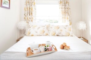 A neatly made bed with a tray of breakfast items, including croissants and a teapot, in a bright room with floral curtains and fluffy white decorations. - Lighthouse View - sleeps 4 guests  in 2 bedrooms (Hayle)