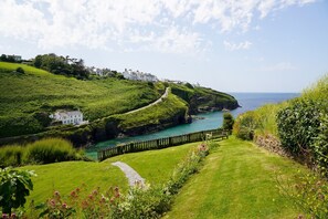 A coastal landscape with a grassy path, a wooden fence, and a white building. - Lower Tregudda Apartment - sleeps 8 guests  in 5 bedrooms (Port Gaverne)