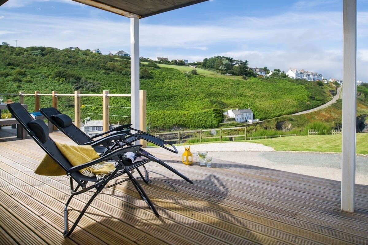 A wooden deck with two lounge chairs, a lantern, and a view of a hillside with houses.