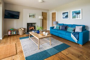 Ein Wohnzimmer mit einem blauen Sofa, einem Holztisch, einem Kamin und einem an der Wand montierten Fernseher.