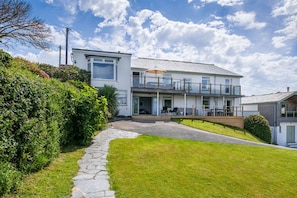Ein modernes, zweistöckiges Haus mit einem Kiesweg, der zum Eingang führt, einem Balkon mit Gartenmöbeln und einem gepflegten Rasen.
