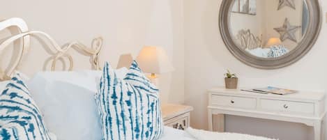 Un dormitorio con cama, almohadas, mesita de noche, lámpara, cómoda y espejo.