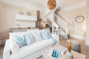 Ein modernes Wohnzimmer mit einem weißen Sofa, einem Couchtisch und einer Treppe, die zur Küche führt.