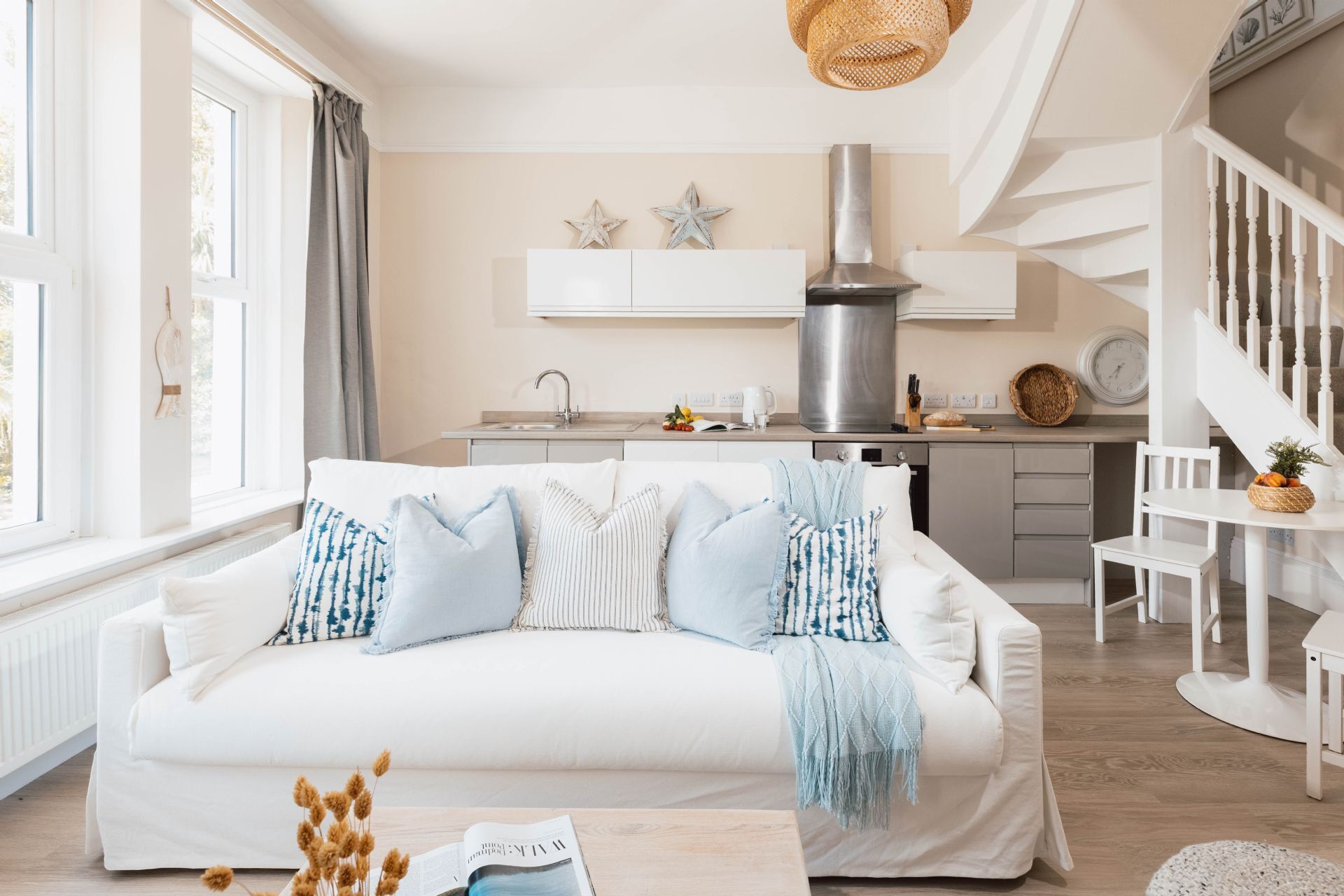 Un salon moderne avec un canapé blanc, un coin cuisine et un escalier.