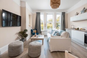 Ein modernes Wohnzimmer mit einer Couch, Hocker, einem Couchtisch und einem Fernseher.