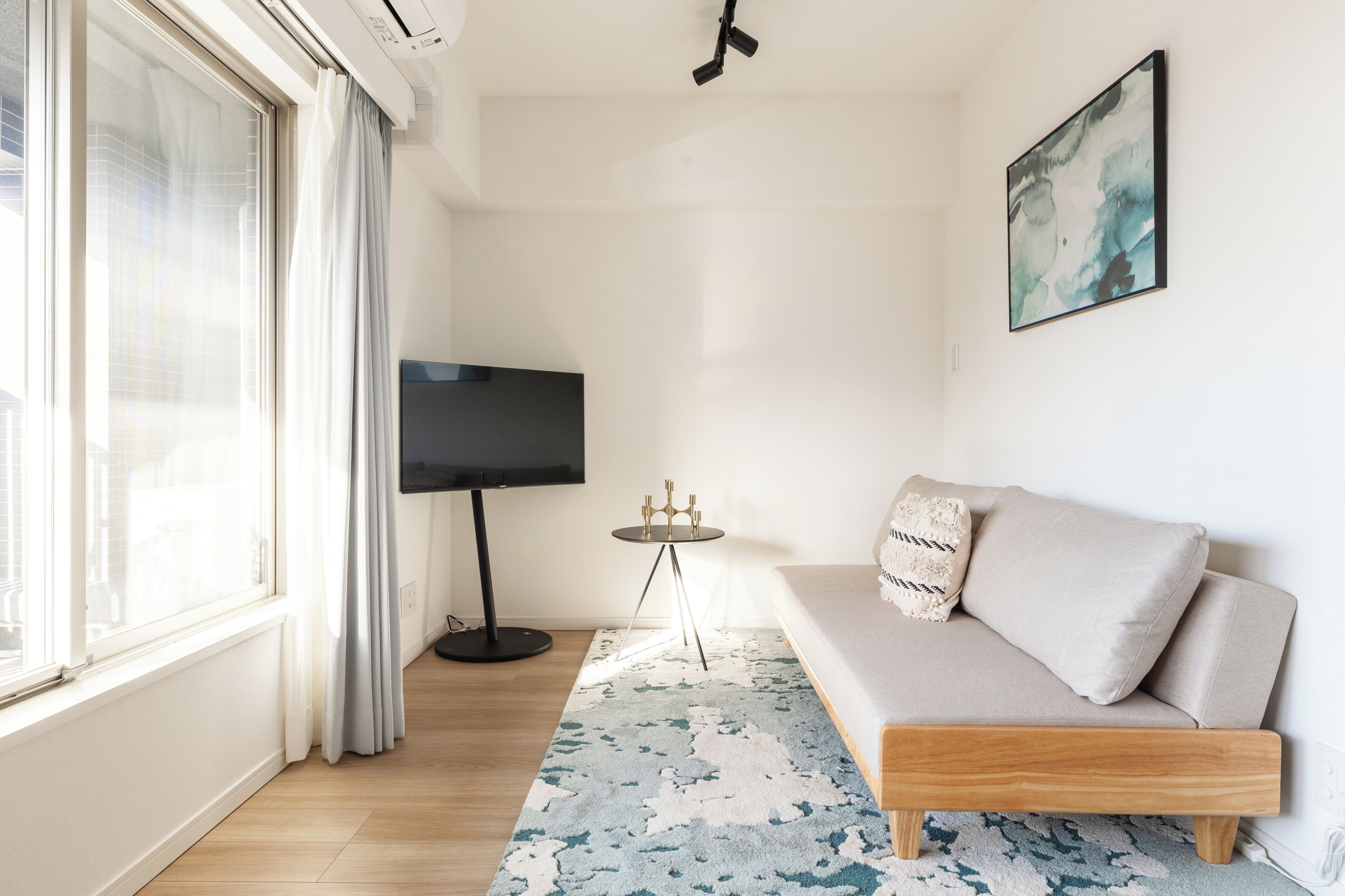 A modern living room with a sofa, a flat-screen TV, a small table, and a patterned rug.