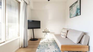 A modern living room with a sofa, a flat-screen TV, a small table, and a patterned rug.