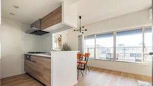 A modern kitchen with wooden cabinets, a built-in stove, and a large window overlooking a balcony. - Dash Living Asakusa East (Higashikomagata, Sumida City)