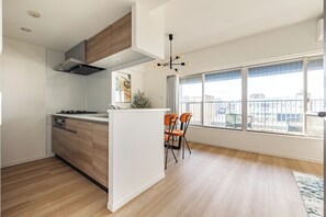 A modern kitchen with wooden cabinets, a built-in stove, and a large window overlooking a balcony. - Dash Living Asakusa East (Higashikomagata, Sumida City)