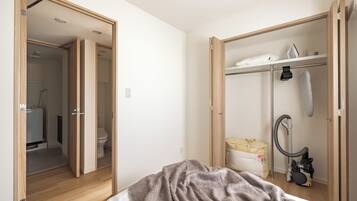 A bedroom with a bed, a closet with a hanging iron, and a vacuum cleaner.
