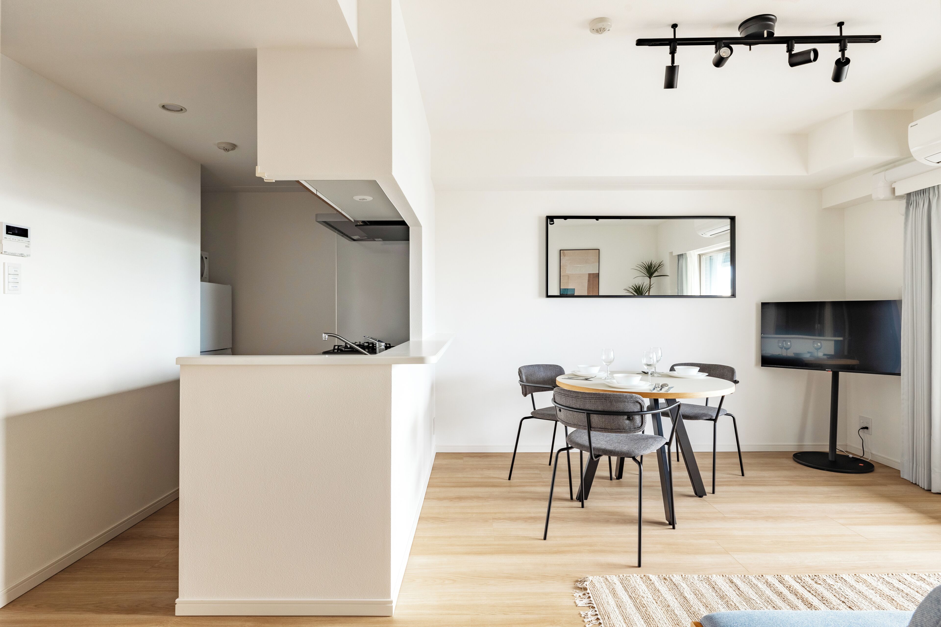 A modern kitchen with a central island, a dining area with a round table and chairs, and a flat-screen TV mounted on the wall.