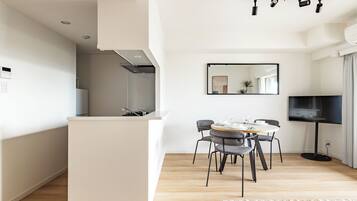 A modern kitchen with a central island, a dining area with a round table and chairs, and a flat-screen TV mounted on the wall.