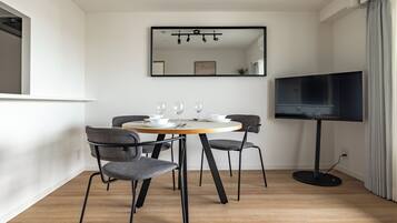 A modern dining area with a round table, four chairs, a flat-screen TV, and a mirror on the wall.
