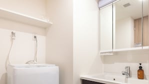 A bathroom with a white washing machine, dark wooden cabinets, a sink with a mirror, and a bottle of soap. - Dash Living Asakusa East (Higashikomagata, Sumida City)