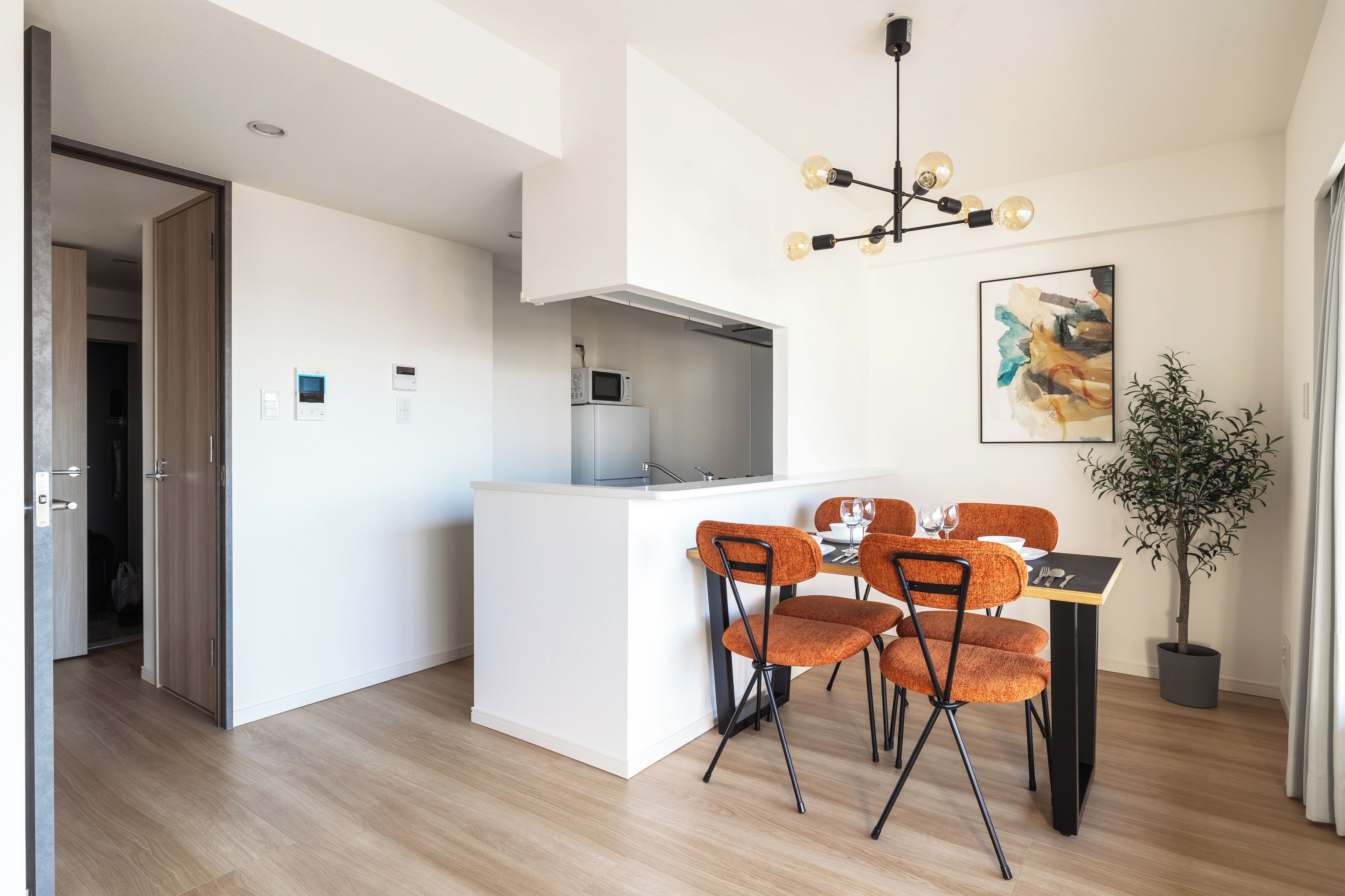 A modern kitchen with a white island, a dining area with orange chairs, and a potted plant.