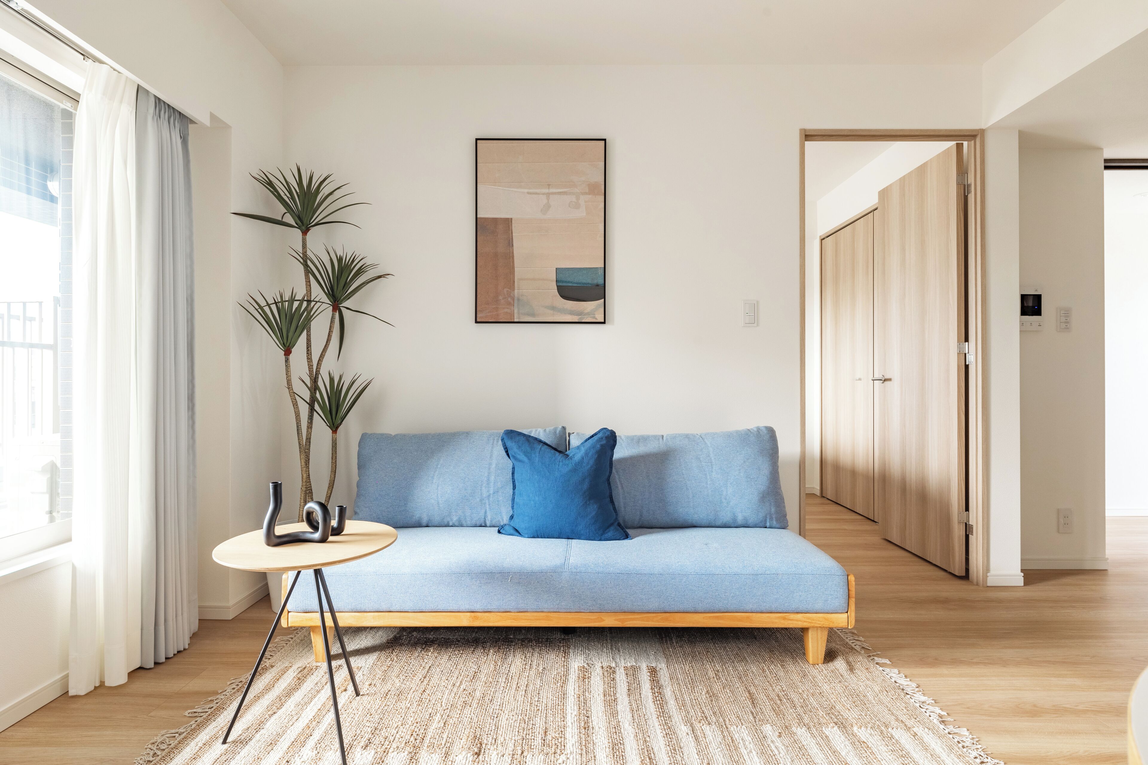 A modern living room with a light blue sofa, a round side table, and a large plant.