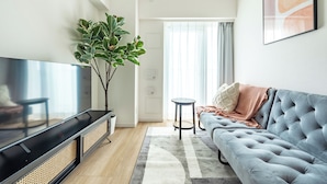 A modern living room with a flat-screen TV, a grey sofa, a large plant, and a small round table. - Dash Living Asakusa East (Higashikomagata, Sumida City)