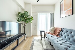 A modern living room with a flat-screen TV, a grey sofa, a large plant, and a small round table. - Dash Living Asakusa East (Higashikomagata, Sumida City)