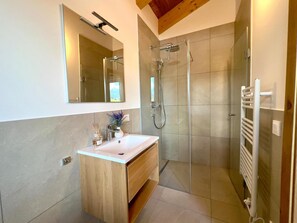 A modern bathroom with a glass shower enclosure, a wooden vanity with a white sink, and a large mirror above the vanity. - Beautiful spacious chalet with sauna and hottub (Sankt Lambrecht)