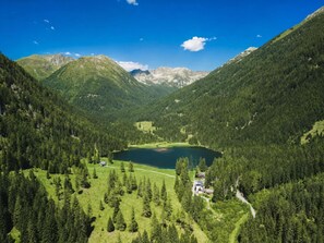 Un paysage montagneux avec un lac, des zones boisées et quelques bâtiments.