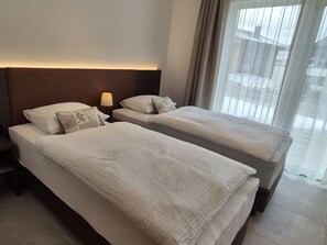A hotel room with two single beds, a nightstand with a lamp, and a large window with curtains. - Beautiful spacious chalet with sauna and hottub (Sankt Lambrecht)