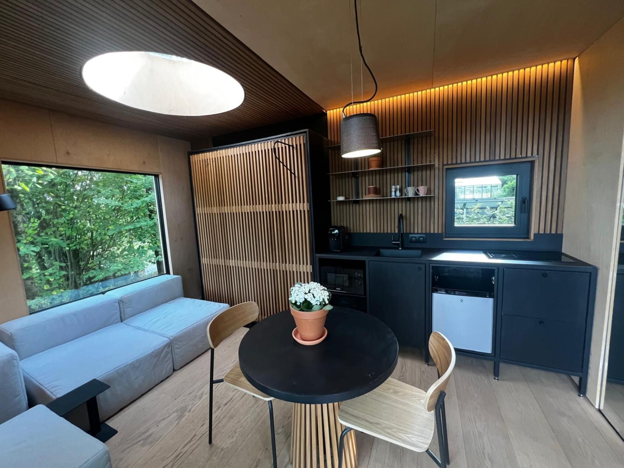 Een moderne keuken met een eethoek, een inbouwoven en een raam met uitzicht op groen.
