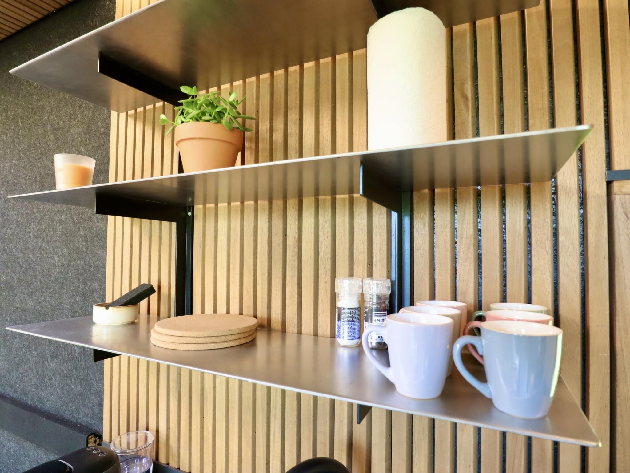 Een plank met een potplant, een glas, een spons, een bak en verschillende mokken.