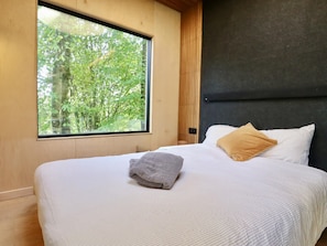 Een slaapkamer met een groot raam, een bed met wit beddengoed, een grijze handdoek en een geel kussen.